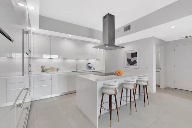 kitchen with visible vents, modern cabinets, a breakfast bar area, island exhaust hood, and a sink