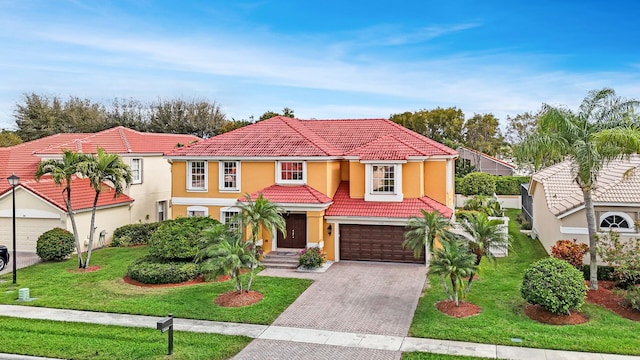 mediterranean / spanish-style home with a tiled roof, a front yard, stucco siding, decorative driveway, and a garage