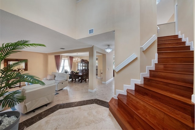 foyer entrance with visible vents, stairway, a high ceiling, an inviting chandelier, and baseboards