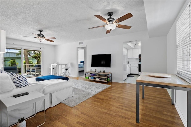 living room with a textured ceiling, wood finished floors, visible vents, and a ceiling fan