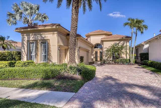 mediterranean / spanish home with decorative driveway, a tiled roof, an attached garage, and stucco siding