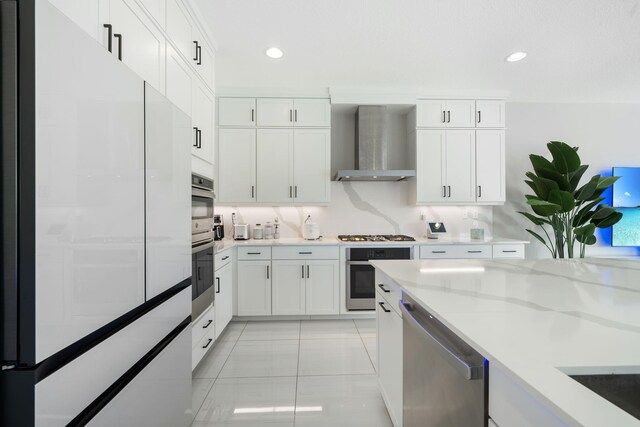 kitchen featuring wall chimney exhaust hood, appliances with stainless steel finishes, light stone countertops, white cabinetry, and recessed lighting