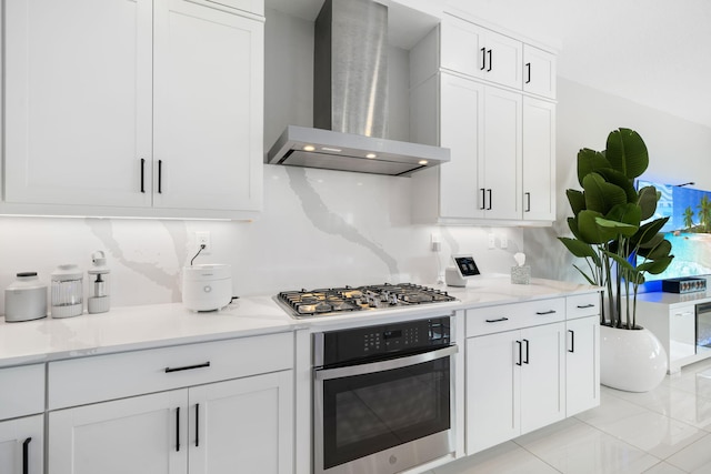 kitchen with wall chimney range hood, appliances with stainless steel finishes, white cabinets, and light stone counters