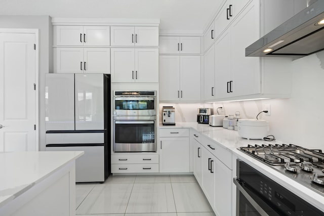 kitchen with appliances with stainless steel finishes, white cabinetry, wall chimney range hood, and light stone counters