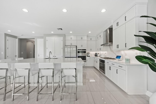 kitchen featuring a spacious island, visible vents, appliances with stainless steel finishes, white cabinets, and wall chimney range hood