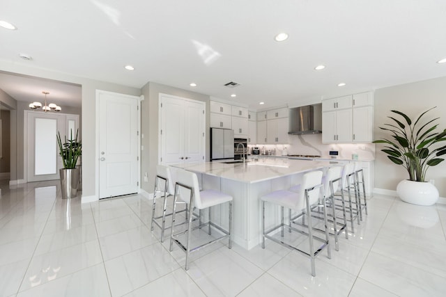 kitchen featuring visible vents, a spacious island, freestanding refrigerator, wall chimney range hood, and white cabinetry