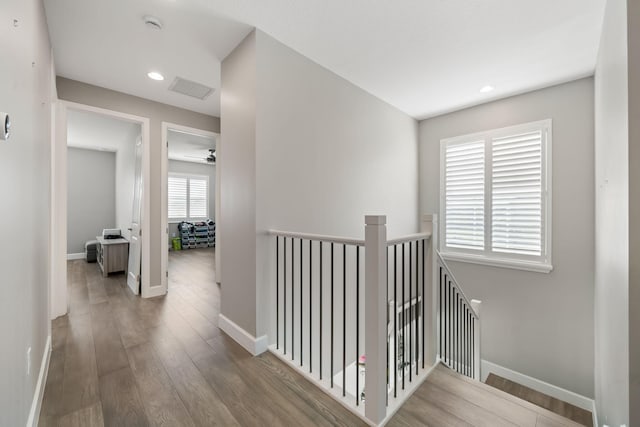 corridor with visible vents, wood finished floors, an upstairs landing, and baseboards