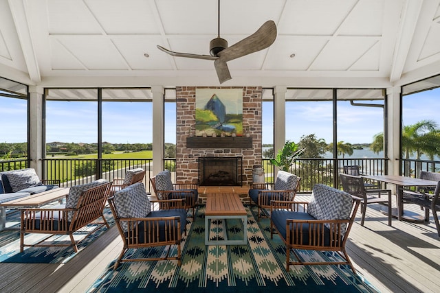 sunroom / solarium with lofted ceiling with beams, ceiling fan, and an outdoor stone fireplace
