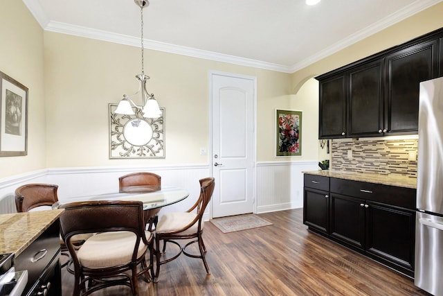 dining area featuring a wainscoted wall, dark wood-type flooring, a chandelier, and crown molding