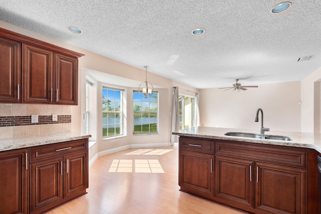 kitchen featuring pendant lighting, a sink, decorative backsplash, and light stone countertops