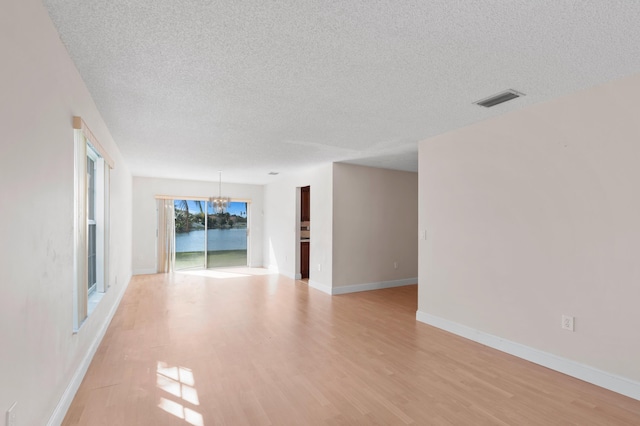 unfurnished room featuring a textured ceiling, a notable chandelier, visible vents, baseboards, and light wood finished floors