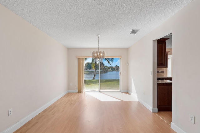 unfurnished dining area with visible vents, an inviting chandelier, a textured ceiling, light wood-type flooring, and baseboards