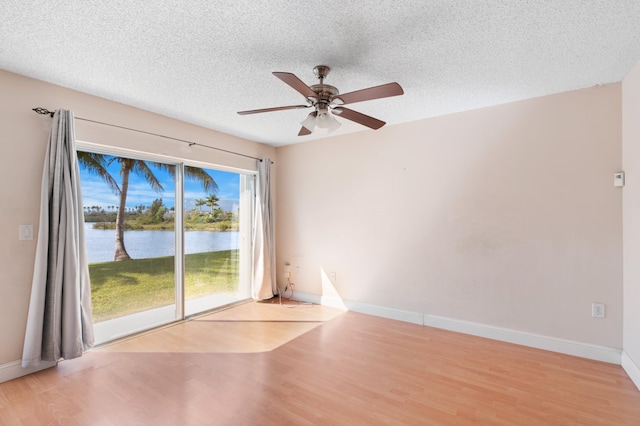 unfurnished room with a water view, light wood-style floors, baseboards, and a textured ceiling