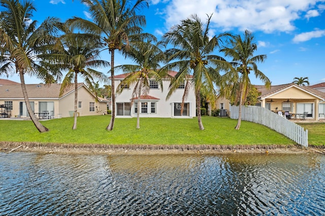 rear view of property with stucco siding, a water view, fence, and a lawn