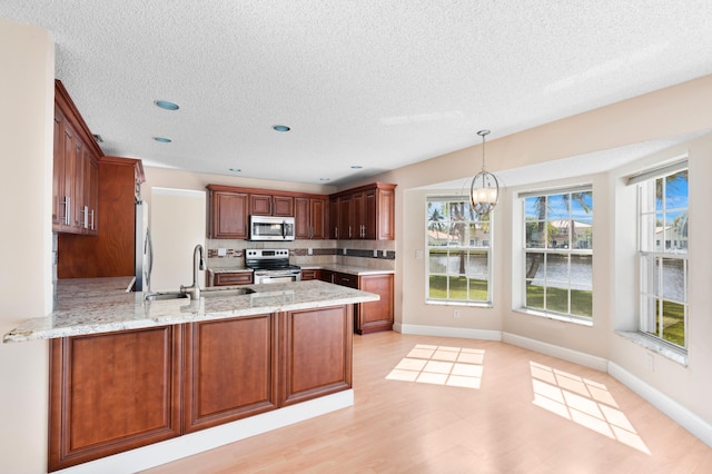 kitchen with a chandelier, stainless steel appliances, a peninsula, a sink, and light stone countertops