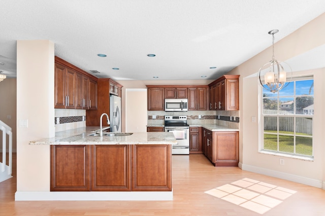 kitchen featuring light stone counters, an inviting chandelier, appliances with stainless steel finishes, a sink, and a peninsula