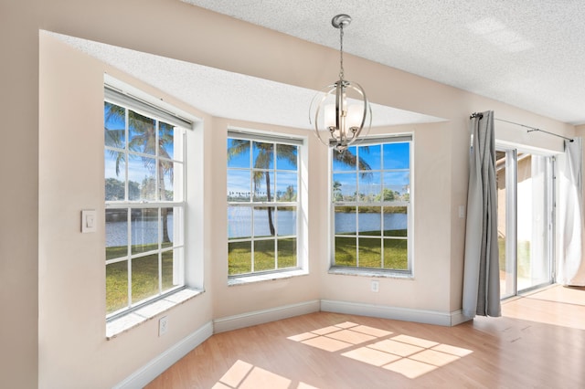 unfurnished dining area featuring a water view, light wood-style flooring, baseboards, and a textured ceiling