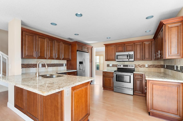 kitchen featuring appliances with stainless steel finishes, brown cabinets, a peninsula, light stone countertops, and a sink