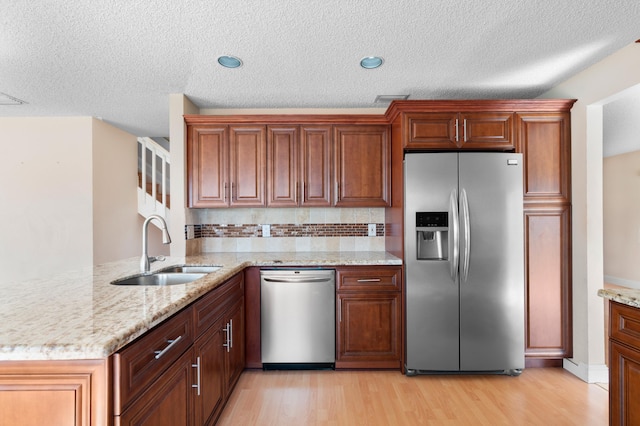 kitchen with stainless steel appliances, a sink, light wood-style flooring, and a peninsula