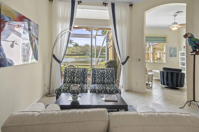 living room featuring plenty of natural light, light tile patterned flooring, a water view, and a ceiling fan