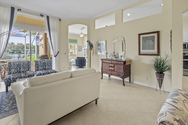 living area with light tile patterned floors, ceiling fan, arched walkways, a water view, and baseboards