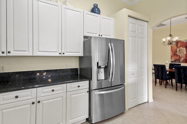 kitchen featuring arched walkways, stainless steel refrigerator with ice dispenser, light tile patterned floors, white cabinetry, and dark stone countertops