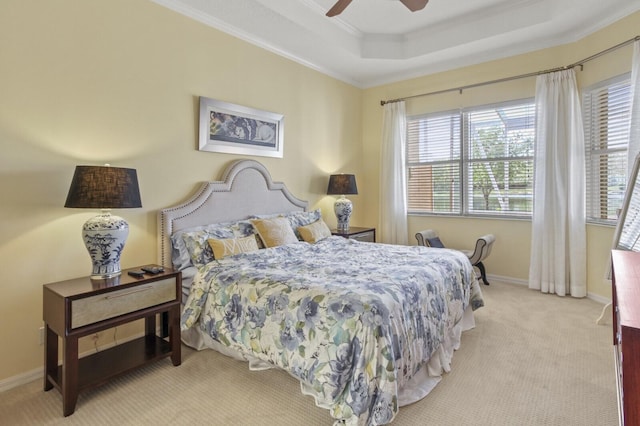 bedroom featuring light carpet, baseboards, a ceiling fan, ornamental molding, and a tray ceiling