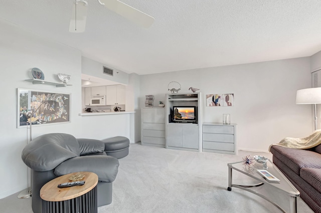 living area featuring a textured ceiling, a multi sided fireplace, visible vents, and light colored carpet