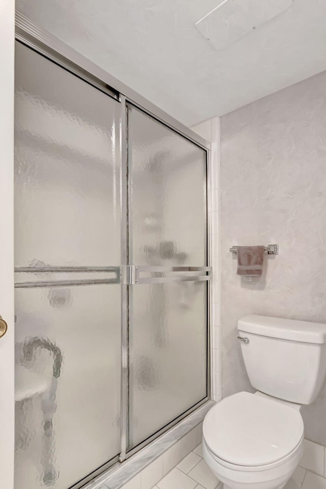 bathroom featuring tile patterned flooring, toilet, and an enclosed shower