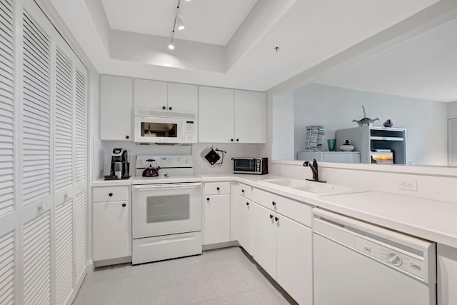 kitchen featuring a raised ceiling, light countertops, white cabinetry, a sink, and white appliances