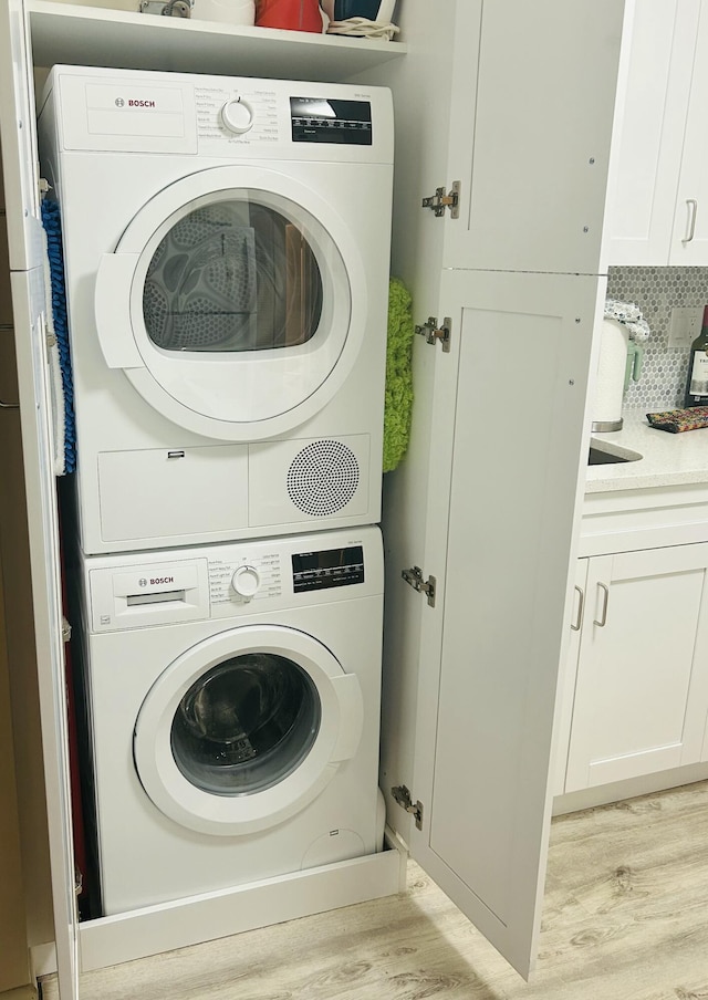 washroom with stacked washer and dryer, light wood finished floors, and cabinet space