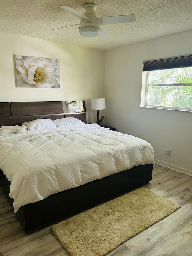 bedroom featuring a textured ceiling, wood finished floors, a ceiling fan, and baseboards