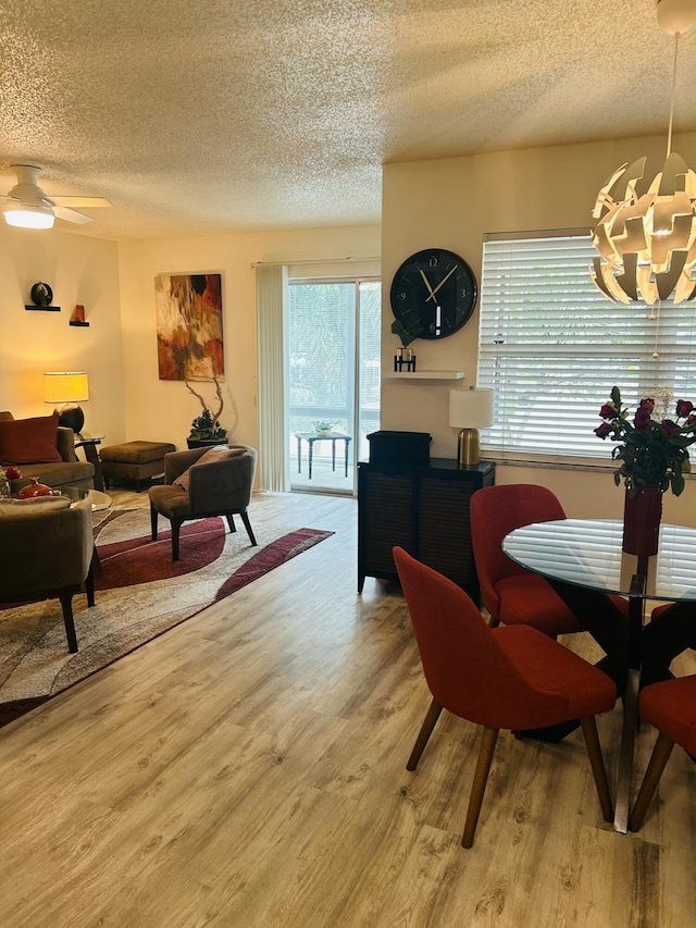 dining space with a textured ceiling, light wood finished floors, and ceiling fan with notable chandelier