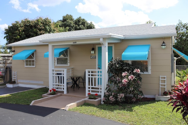 bungalow-style house with a shingled roof, fence, and a front yard