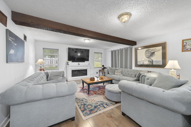 living area featuring beam ceiling, a healthy amount of sunlight, a textured ceiling, and wood finished floors