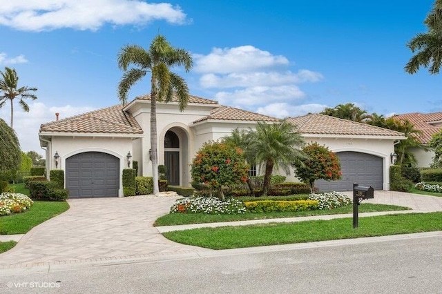 mediterranean / spanish house featuring a garage, decorative driveway, a tiled roof, and stucco siding