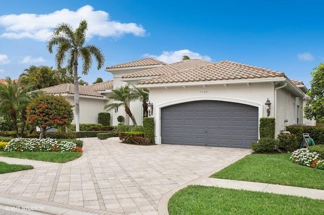 mediterranean / spanish house with a garage, decorative driveway, a tiled roof, and stucco siding