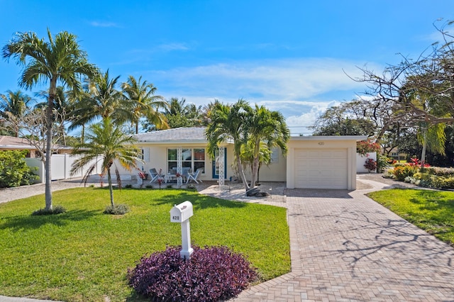 ranch-style house with an attached garage, covered porch, decorative driveway, stucco siding, and a front yard