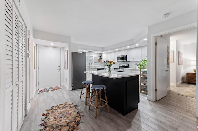 kitchen with white cabinets, light countertops, appliances with stainless steel finishes, backsplash, and a center island