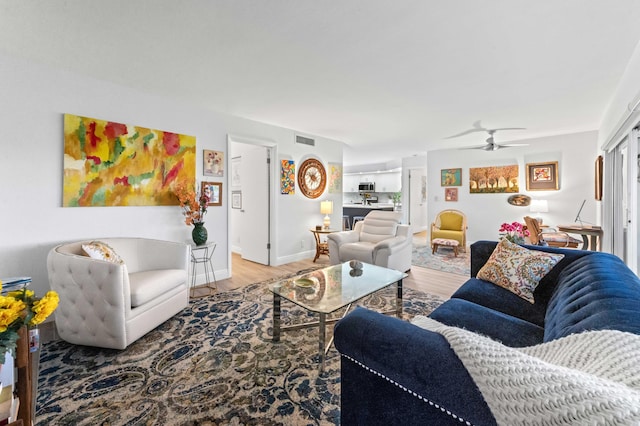 living room with a ceiling fan, visible vents, baseboards, and wood finished floors