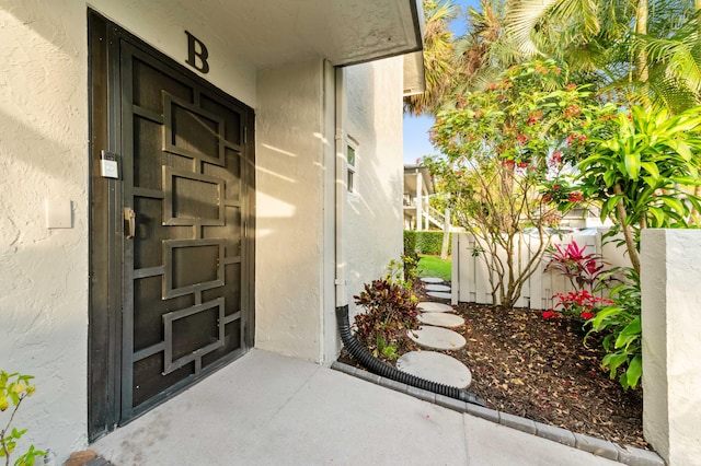 view of exterior entry with fence and stucco siding