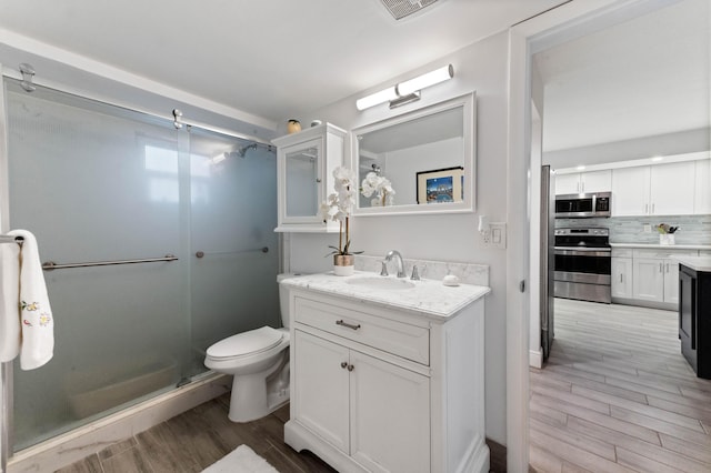 bathroom featuring wood finish floors, toilet, decorative backsplash, a stall shower, and vanity