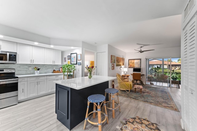 kitchen featuring open floor plan, a center island, stainless steel appliances, light countertops, and white cabinetry