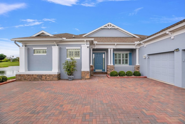 view of front facade featuring covered porch, stone siding, decorative driveway, and a garage