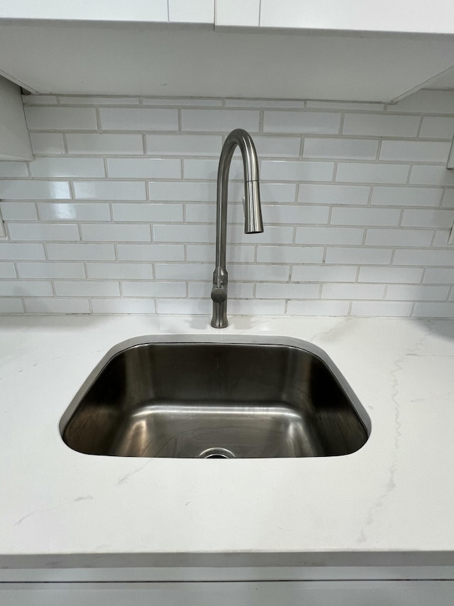 room details featuring light stone counters, a sink, and decorative backsplash