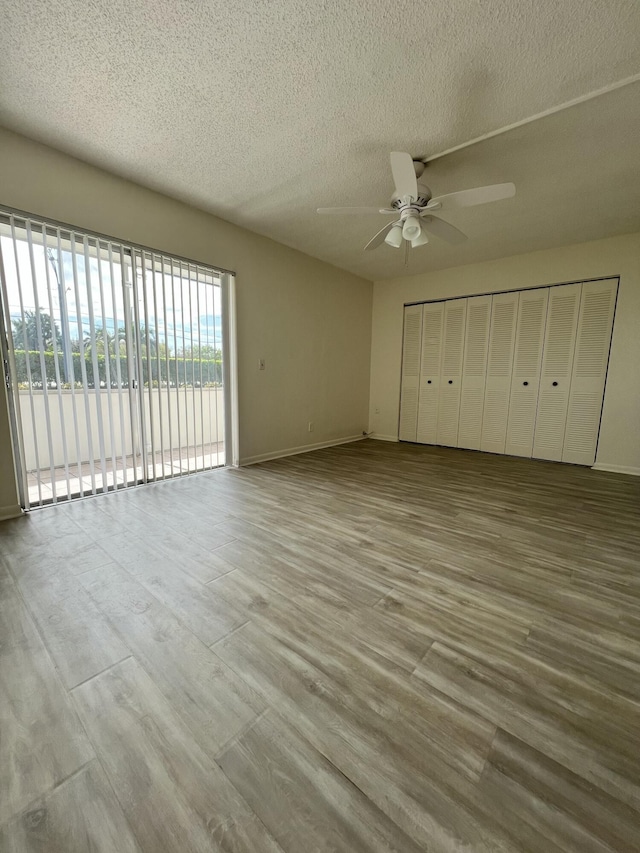 unfurnished bedroom featuring access to exterior, light wood-style flooring, a textured ceiling, and a ceiling fan