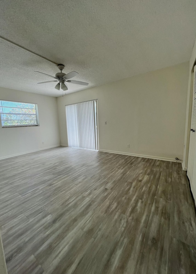 empty room featuring ceiling fan, baseboards, dark wood finished floors, and a textured ceiling