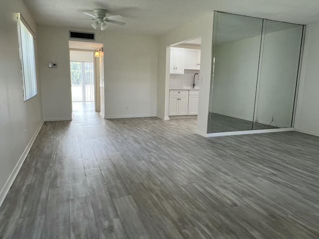 unfurnished living room with ceiling fan, a textured ceiling, a sink, visible vents, and dark wood-style floors