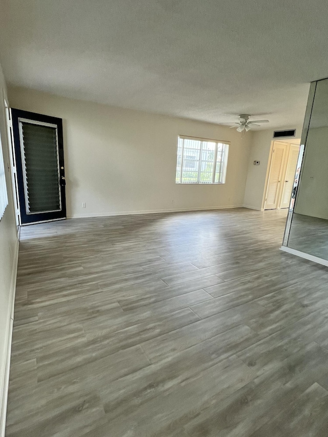 unfurnished living room with a textured ceiling, light wood finished floors, a ceiling fan, and baseboards