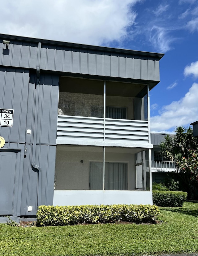 view of side of property with a yard, board and batten siding, and a balcony